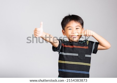 Little cute kid boy 5-6 years old smile brushing teeth and show thumb up finger for good sign in studio shot isolated on white background, happy Asian children, Dental hygiene healthy concept