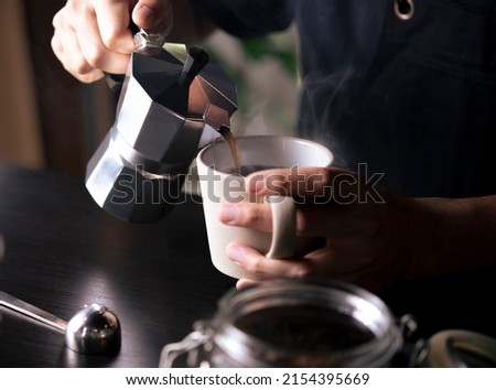 Barista pouring coffee from moka pot coffee maker to a coffee cup. Hand holding Italian classic moka pot pouring coffee. Royalty-Free Stock Photo #2154395669