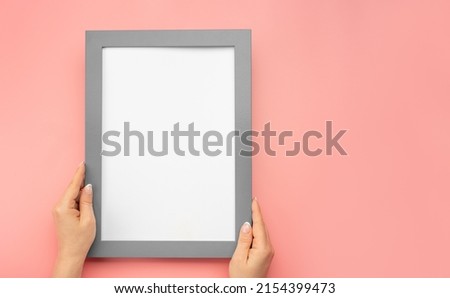 Hanging a photo frame mockup on pink wall. Picture frame mockup. Woman hold blank diploma frame on pink wall background. Cropped hand of woman holding picture frame against pink wall. copy space
