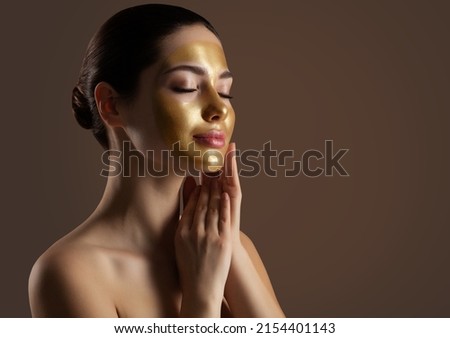 Facial peeling Golden Mask. Woman with Gold Lifting Face Mask over Dark Background. Beauty Model enjoying Skin Care Spa Cosmetology with closed Eyes. Women Anti Aging Cosmetics