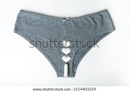 Gray women's panties and white cotton sanitary tampon and hearts as mestrual drops on a white background, top view, minimalism. Menstrual cycle. Feminine hygiene and health care