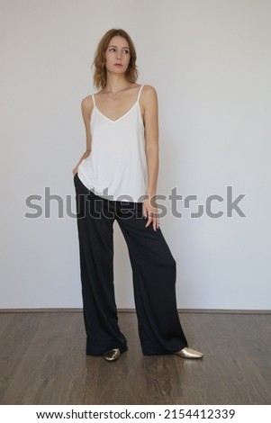 Female model wearing white camisole cotton top and black trousers. Classic and simple summer fashion. Studio shot. Royalty-Free Stock Photo #2154412339