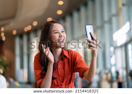 happiness asian female woman smile hand wave give a kiss to family via video call smartphone device social distancing greeting with blur mall background new normal lifestyle