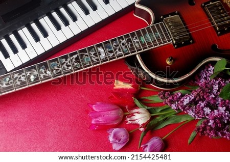 Electric guitar, synthesizer keyboard and a bouquet of tulips on a red table.