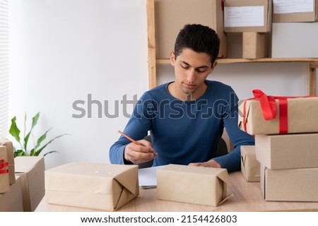 Online salesman young muslim salesman checks online order, checks goods in stock, package, mail delivery. arab man starts small business in home office. copy space.
