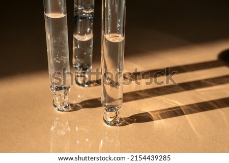 Three pipettes of cosmetic gel on a beige background.