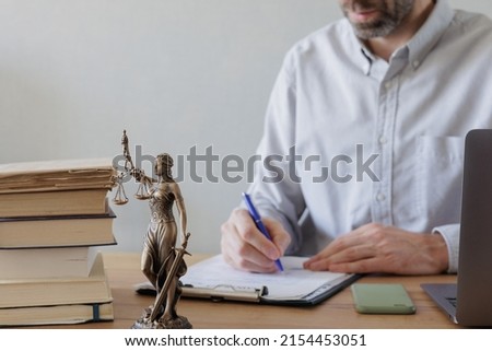 an adult male lawyer in the office checks the contract or advises the client. selective focus, statuette of the goddess of justice Themis. a lawyer signs a contract for the sale of real estate
