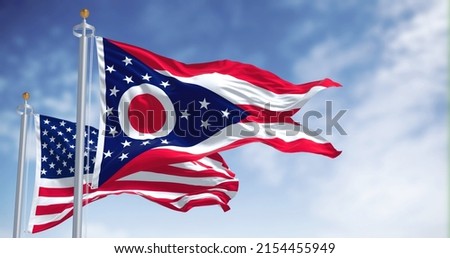 The Ohio state flag waving along with the national flag of the United States of America. In the background there is a clear sky. Ohio is a state in the Midwestern region of the United States Royalty-Free Stock Photo #2154455949