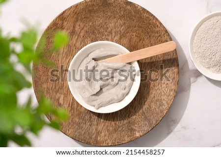 Bowl with gray cosmetic clay cream on wooden tray - mineral bentonite facial mask. Skincare beauty concept. Top view Royalty-Free Stock Photo #2154458257