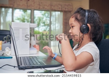 Smiling adorable little girl with headphones using laptop computer for distance learning while staying at home on self isolation. Online education in the period of the epidemic covid 19 concepts.