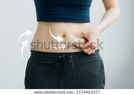 Skinny fat woman figure in fitness clothes touches stomach. Abdominal fat and dieting concept. Massaging marks. Royalty-Free Stock Photo #2154463227
