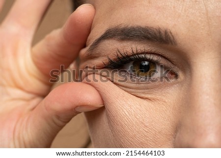 woman showing her eye wrinkles with her fingers on a white background. Royalty-Free Stock Photo #2154464103