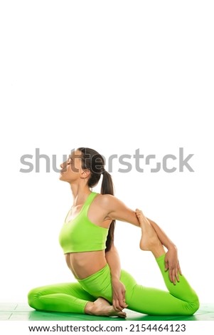 Young sporty attractive woman practicing yoga, doing Mermaid exercise, Eka Pada Rajakapotasana pose, working out, wearing sportswear, green  pants and top, indoor full length, white background..