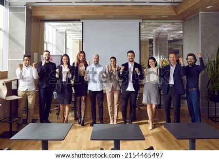 Happy business team celebrating great achievements and teamwork. Multriacial group of cheerful colleagues standing by office projection screen cheering after successful presentation at work meeting Royalty-Free Stock Photo #2154465497