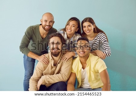 Portrait of smiling group of diverse multiracial young people on light blue background. Best friends posing together looking at camera. Concept of friendship between different races and nationalities.