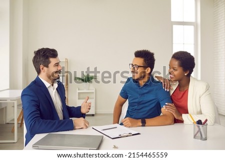 Happy ethnic couple clients talk with real estate agent sign agreement buy house together. Smiling multiracial man and woman put signature make deal with broker or realtor. Realty, rent concept.