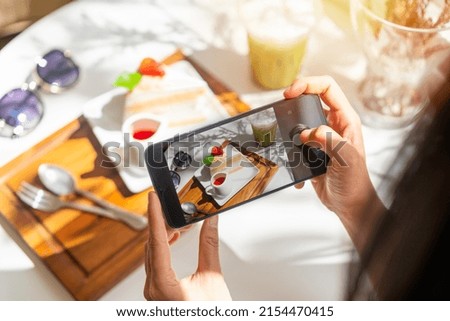 Young woman taking photo of dessert with smart phone for social media in restaurant while traveling