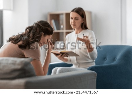 psychology, mental health and people concept - psychologist with notebook talking to stressed woman patient at psychotherapy session Royalty-Free Stock Photo #2154471567
