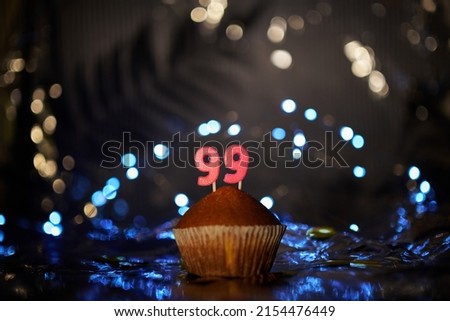 Fresh tasty homemade vanilla cupcake with number 99 ninety nine on aluminium foil and blurred bright background in minimalistic style. Digital gift card birthday concept. High quality image