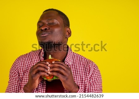 young african american man eating hamburger isolated on yellow background