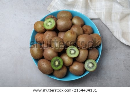 Fresh ripe kiwis in bowl on light grey table, top view