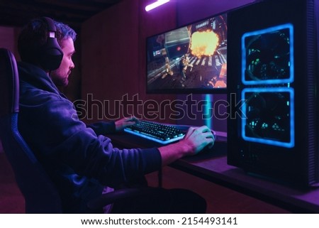 Young concentrated cyber sportsman playing in FPS video game on his personal computer in dark neon room. Pro gamer participating in online esport competition. Cyber games championship event concept Royalty-Free Stock Photo #2154493141
