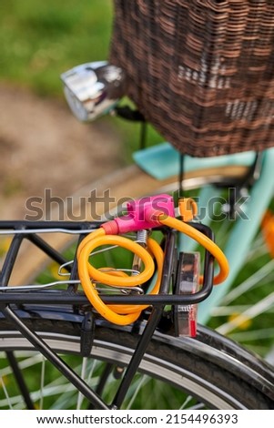 A vertical closeup of the back of a bike with an orange steel wire lock