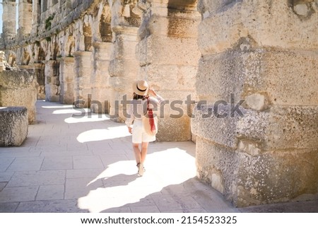 woman in hat stands and looking on Coliseum in Pula Croatia. travel concept.Young woman enjoy summer Italian vacation in Europe. Royalty-Free Stock Photo #2154523325