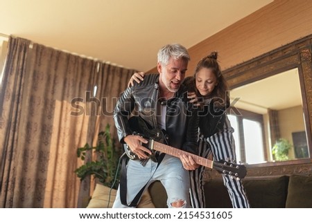 Father rock guitarist having fun and and dancing with his teenage daughter at home. Royalty-Free Stock Photo #2154531605