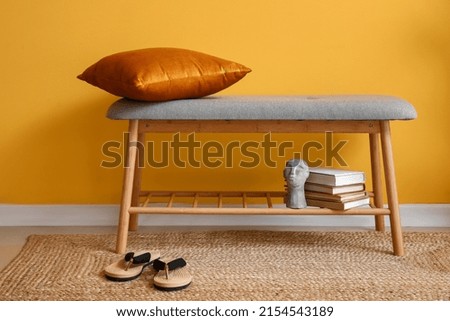 Comfortable bench with pillow, books and flip flops near yellow wall