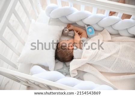 Cute little child with toy and baby monitor sleeping in crib Royalty-Free Stock Photo #2154543869