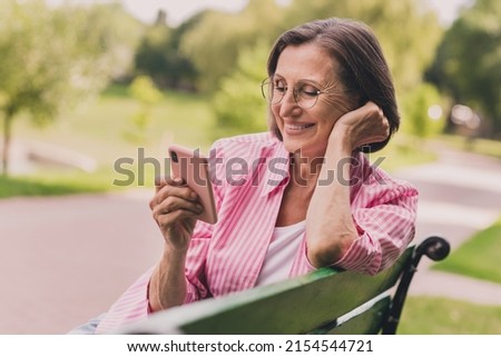 Photo of sweet pretty retired woman dressed striped shirt reading modern device outside countryside landscape