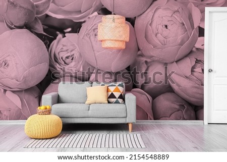 Comfortable sofa and stylish pouf with chandelier near wall with printed flowers