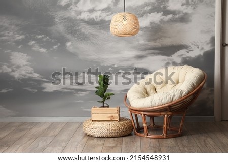 Stylish armchair with houseplant and chandelier near painted grey wall in room