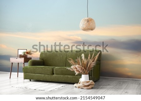 Stylish sofa with floral decor and chandelier near painted wall in room
