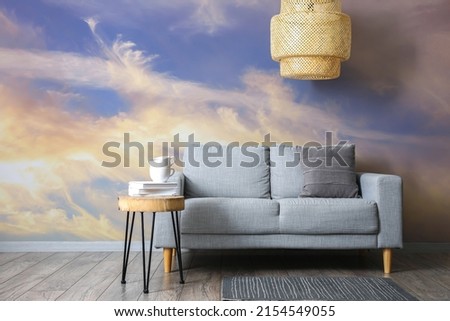 Comfortable sofa with table and stylish chandelier near wall with printed sky