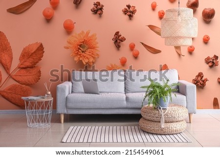 Comfortable sofa with houseplant and stylish chandelier near wall with printed floral decor