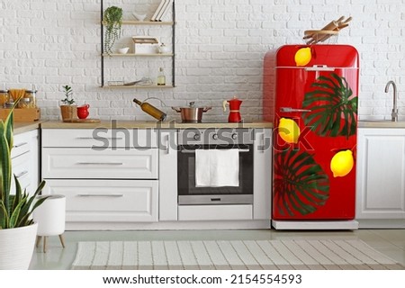 Red refrigerator with print of tropical leaves in interior of modern kitchen