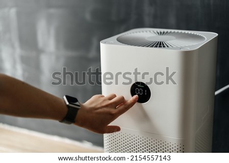 woman's hand presses the touch screen button to start an air purifier in her apartment. Human Health and Technology. Royalty-Free Stock Photo #2154557143