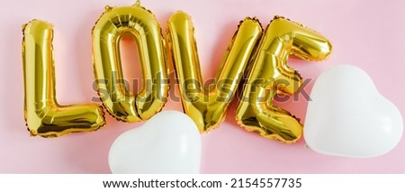 Inscription LOVE foil inflatable golden ballon on the pink background with white hearts. Love, romance and Valentines day concept. Flat lay