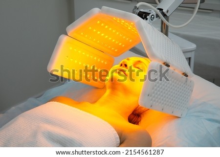 An elderly woman undergoes a facial rejuvenation procedure. Woman face lt Red light treatment At beauty clinic. Cosmetology.