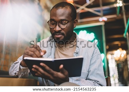 Smart black student writing education essay story in notepad, intelligent African American male making notes of planning in notebook for organization - learning and studying in coworking space Royalty-Free Stock Photo #2154563235