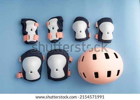 Top view of roller skates protective gear set - knee, elbow and wrist pads and helmet in pink colors. Blue background flat lay 