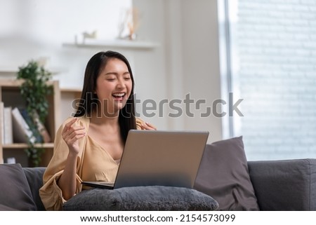 beautiful asian young woman wear casual sit on couch using computer laptop entertain with social media relax smile and laughing.Freelance woman working online sale marketing,Shopping online at home.