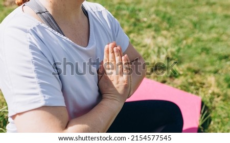 Young smiling attractive redhead woman practicing yoga, girl doing Ardha Padmasana exercise and meditating in Half Lotus pose with namaste on nature background, working out