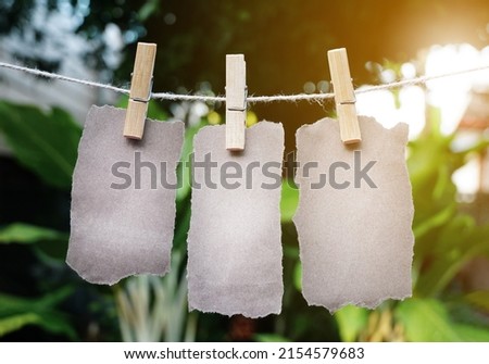 empty Brown paper torn three sheets or ripped pieces hanged with clothes pegs on rope at the green garden.                 