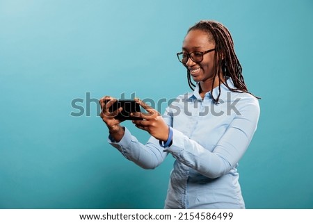 Happy smiling heartily woman modern smartphone touchscreen device enjoying watching funny videos on internet. Confident joyful young adult with mobile cellphone browsing webpage on blue background.