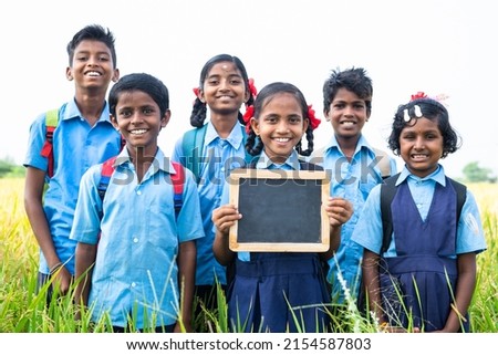 Village teenage kids showing empty slate board by looking at camera at farmland - concept of advertisement, education and friendship Royalty-Free Stock Photo #2154587803