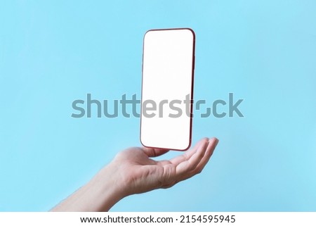 Smartphone floating in palm of hand supports with a blank display screen , Mobile phone isolate on blue green background Royalty-Free Stock Photo #2154595945