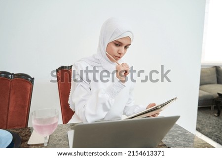 Muslim woman working on laptop and taking notes at home
